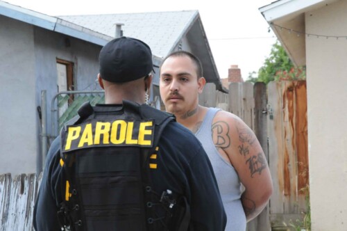 Parole officer conducting home visit with parolee in residential neighborhood, demonstrating community supervision and field monitoring responsibilities