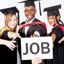 Diverse group of college graduates in caps and gowns smiling and holding JOB sign representing successful psychology degree career outcomes
