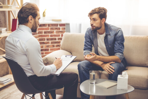 Licensed therapist conducting individual therapy session with male client in professional counseling office with modern comfortable setting