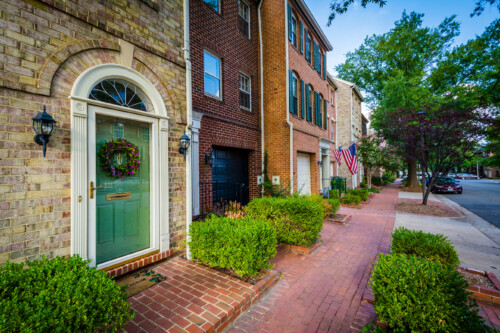 A charming residential street in Virginia, featuring brick townhouses with a well-maintained sidewalk, lush greenery, and American flags, representing the welcoming communities where licensed counselors can make a difference.